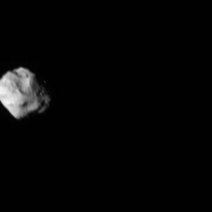 Dinkinesh, a diamond-shaped asteroid taking up about a third of the height of the image, is on the left-hand side. It's lit from the left. At the very right of the image is Selam, two small rocks are connected to each other. There's a black line in between them which is a shadow from the left-hand rock.