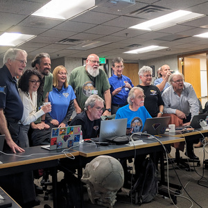 Many people stand around tables spanning across the room, while looking to the right and with delighted expressions. Not pictured: the first image of Dinkinesh.