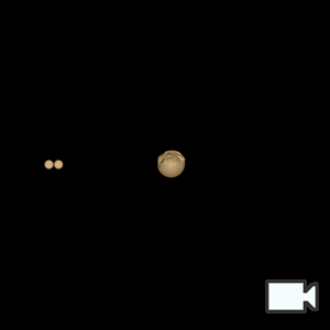 A simulated top down view of the binary asteroid Selam rotating clockwise around its host asteroid Dinkinesh. Selam is two rocks connected to each other with a black line in between them. Dinkinesh is in the center rotating clockwise, with only one side of the simulated sphere rendered as the asteroid's surface. Both asteroids are a tan/beige color.