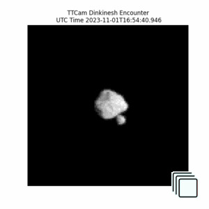 Dinkinesh, a diamond-shaped asteroid in the center, and Selam, a smaller asteroid of two connected rocks on the left, approach, pass across, then depart away from the camera. As they approach, the shape of both asteroids get clearer and the lighting is harsh from the right.  As the camera passes across them, Selam moves behind Dinkinesh to the right of it. As they depart, the binary shape of Selam (two connected rocks separated by a black line) is clear. The images are pixelated. Above the movie, there is the text ''TTCam Dinkinesh Encounter'' and the UTC Time of the counter.