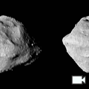 Two almost identical gifs of Selam (two connected rocks) side by side. It is rotating left to right. One of its nodes is moving behind to foreground rock. It is lit from the right with harsh shadows.